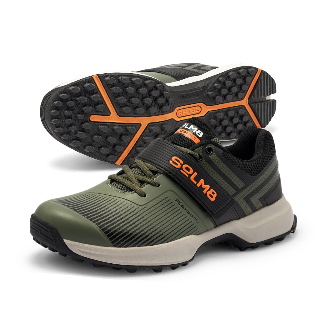Olive green SOLM8 cricket shoes with black and orange accents, featuring a high-traction sole design